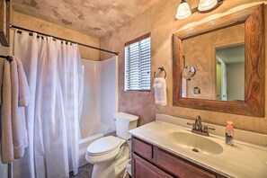 Een badkamer met douchegordijn, toilet, wastafel en spiegel.
