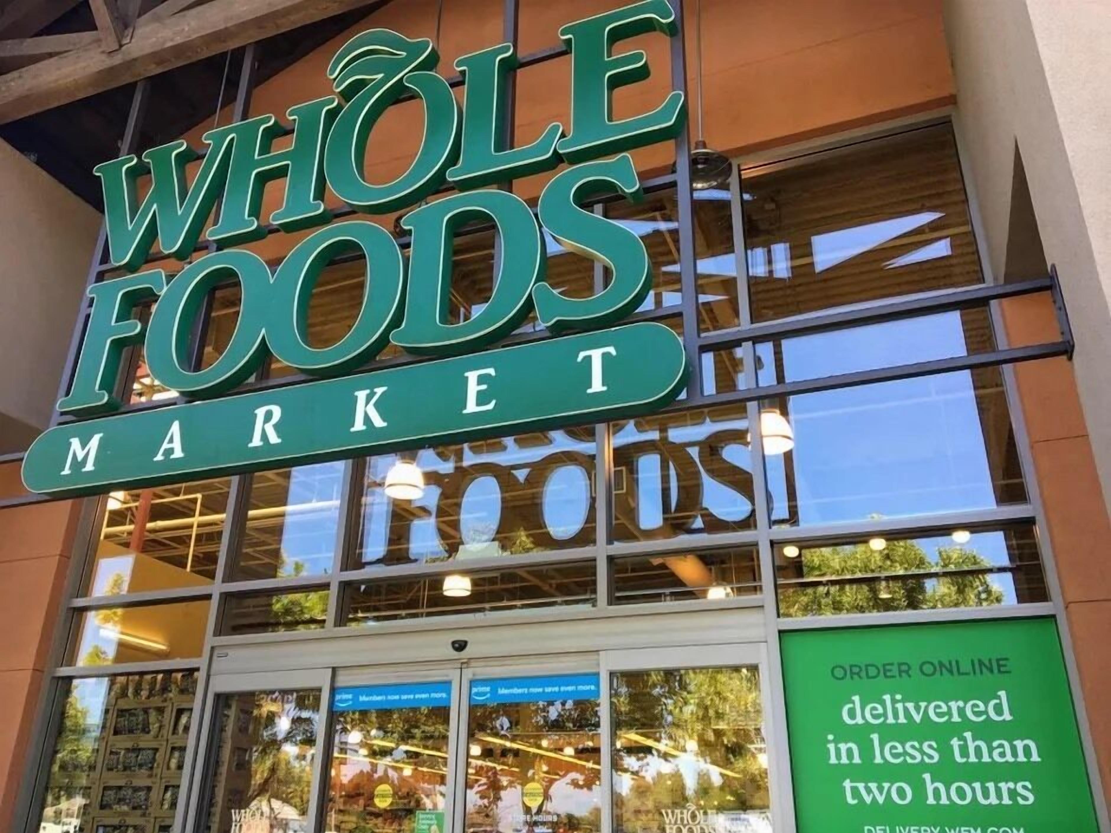 A Whole Foods Market storefront with large windows and a sign indicating online order delivery in less than two hours.