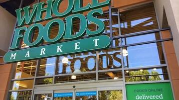 A Whole Foods Market storefront with large windows and a sign indicating online order delivery in less than two hours.