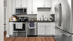 A modern kitchen with white cabinets, stainless steel appliances, and a wooden floor.