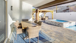Un patio exterior con piscina, mobiliario de mimbre y una pérgola.