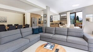 Uma sala de estar moderna com um sofá modular cinza, uma mesa de centro redonda e uma área de jantar com mesa e cadeiras de madeira.
