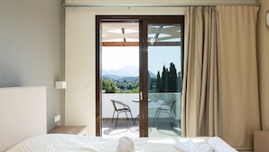 Quarto de hotel com cama, varanda e vista para o campo, além de porta de correr de vidro.