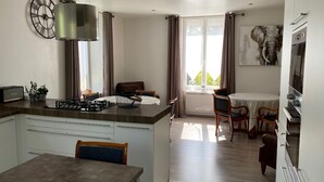 A modern kitchen with a central island, dining area with a table and chairs, and a large window with curtains. - GITE***** DE LUXE VOSGES: CHEZ LIVIA (Bruyères)