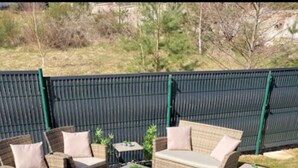 An outdoor patio area with wicker furniture, including sofas and a coffee table, surrounded by a green fence. - GITE***** DE LUXE VOSGES: CHEZ LIVIA (Bruyères)