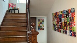 A staircase with wooden steps and a balustrade, leading to a room with a colorful quilted wall hanging and a bench. - GITE***** DE LUXE VOSGES: CHEZ LIVIA (Bruyères)
