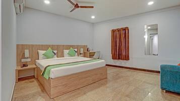 A modern hotel room with a wooden headboard, a bed with green and white bedding, a desk with a chair, a wooden nightstand, a ceiling fan, and a bathroom mirror.