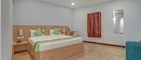A modern hotel room with a wooden headboard, a bed with green and white bedding, a desk with a chair, a wooden nightstand, a ceiling fan, and a bathroom mirror.
