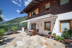 A wooden house with a stone patio, outdoor furniture, and potted plants.