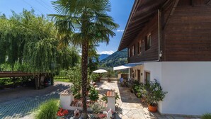Un cortile con patio in pietra, piante in vaso, una palma e un edificio in legno con un'area salotto esterna coperta.