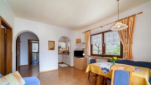 A room with a dining table, chairs, a sofa, a TV, and a kitchen area. - Apartment "Sonnenblume" with Mountain View, Pool, Wi-Fi, Balcony & Garden (Rifiano)
