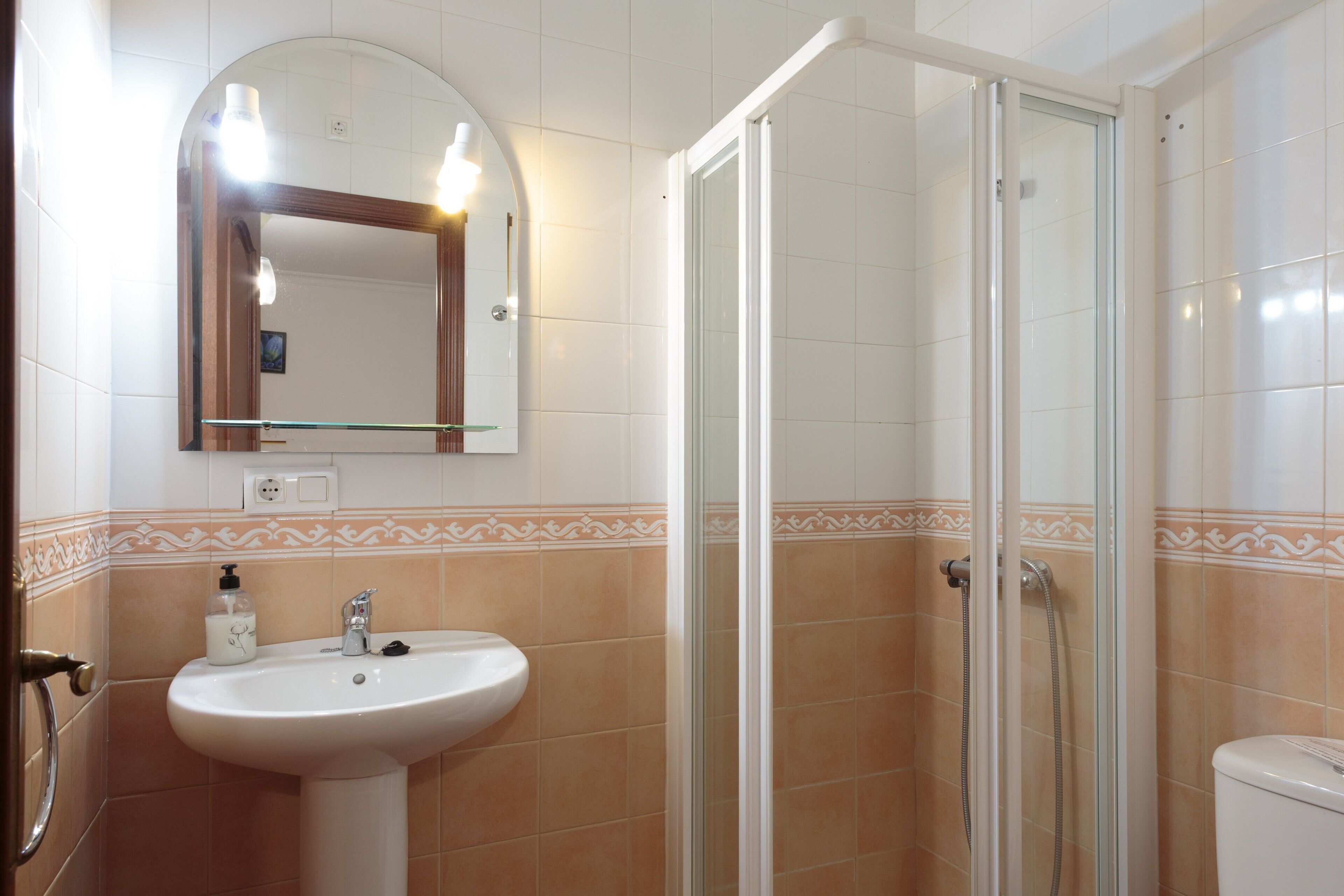 Un baño con lavamanos, espejo, ducha y paredes de azulejos.