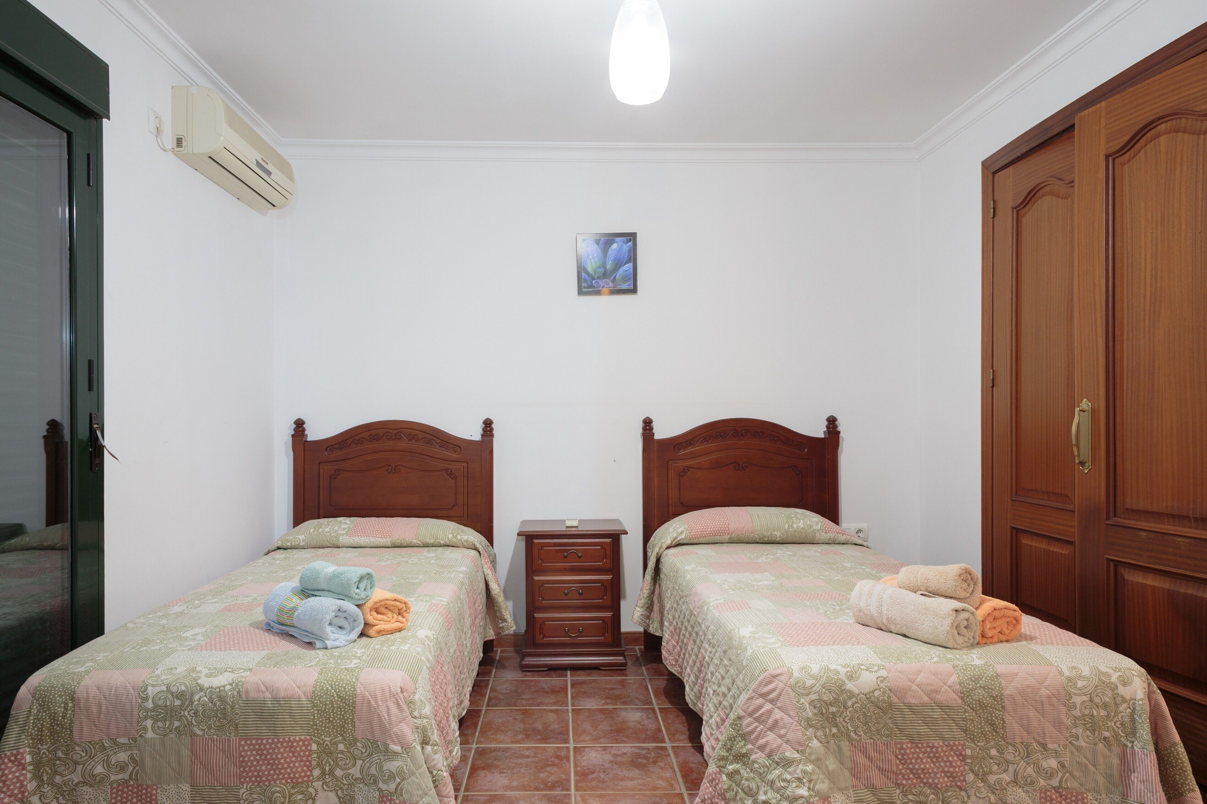 Un dormitorio con dos camas, una mesita de noche, un armario de madera y un equipo de aire acondicionado.