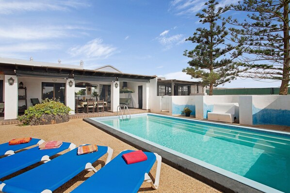A pool area with lounge chairs and a building with a covered patio.