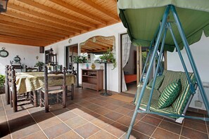 A room with a wooden ceiling, a dining table with chairs, a swing chair, and a mirror.