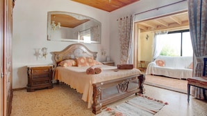 Une chambre à coucher avec un lit en bois, une table de chevet, une commode, un grand miroir et une vue sur un balcon extérieur.
