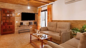 Una sala de estar con techo de madera, un televisor de pantalla plana, un sofá color crema, una mesa de centro y una planta.