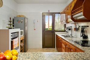 A kitchen with a microwave, oven, refrigerator, wooden cabinets, granite countertop, and a view through the door.