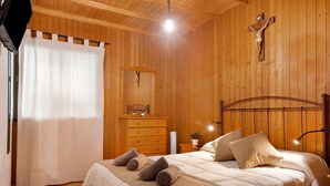 Un dormitorio con paneles de madera, una cama, un aparador de madera, una cruz en la pared y una cortina.
