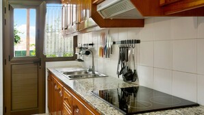 Una cocina con armarios de madera, encimera de granito, pileta de acero inoxidable y estufa eléctrica.