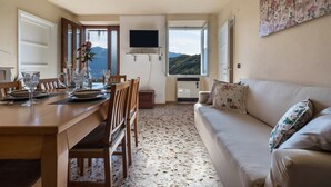 Un coin repas avec une table dressée pour quatre personnes, un canapé, un téléviseur fixé au mur et une fenêtre donnant sur les montagnes.