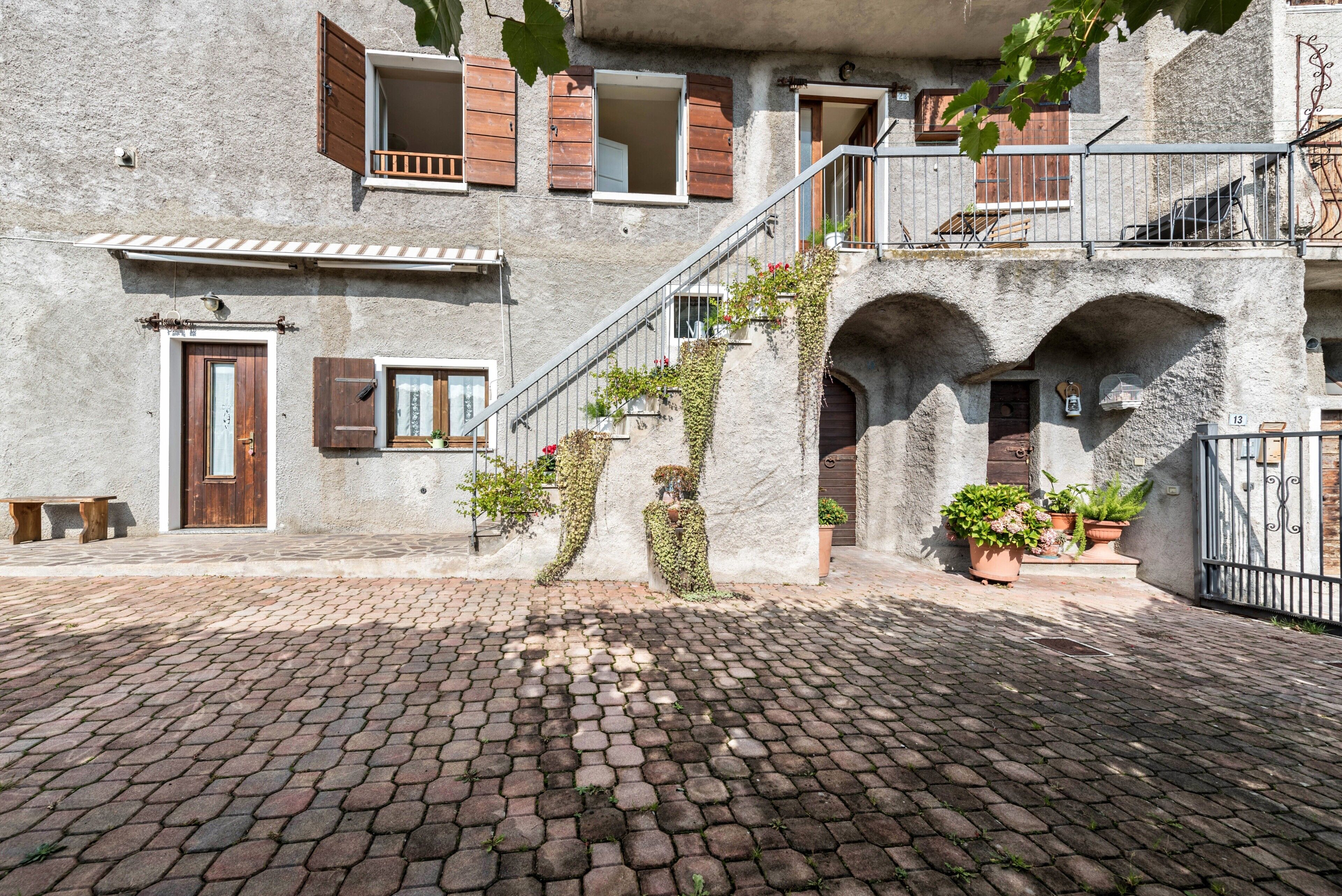 Ein Steingebäude mit einem Kopfsteinpflasterhof, hölzernen Fensterläden und einer Treppe, die zu einer oberen Etage führt.