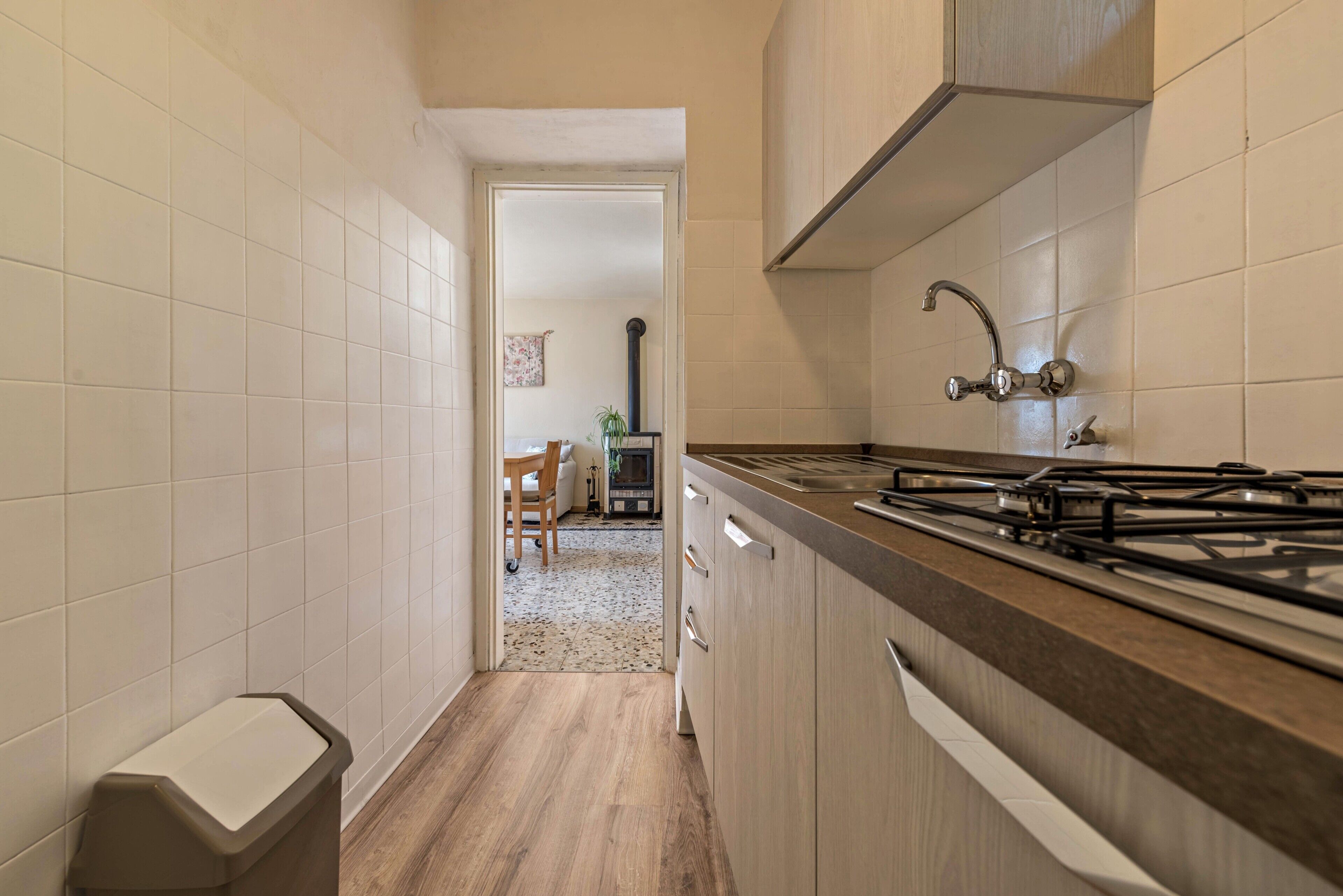 Een keuken met een fornuis, kastjes en een vuilnisbak.