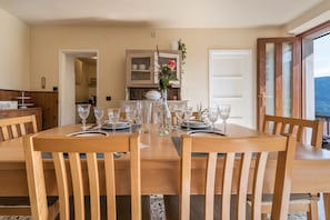 A dining area with wooden chairs and a table set for six with wine glasses and plates. - Apartment "Casa Vacanze Voiandes" with Mountain View, Balcony & Wi-Fi (Tremosine sul Garda)