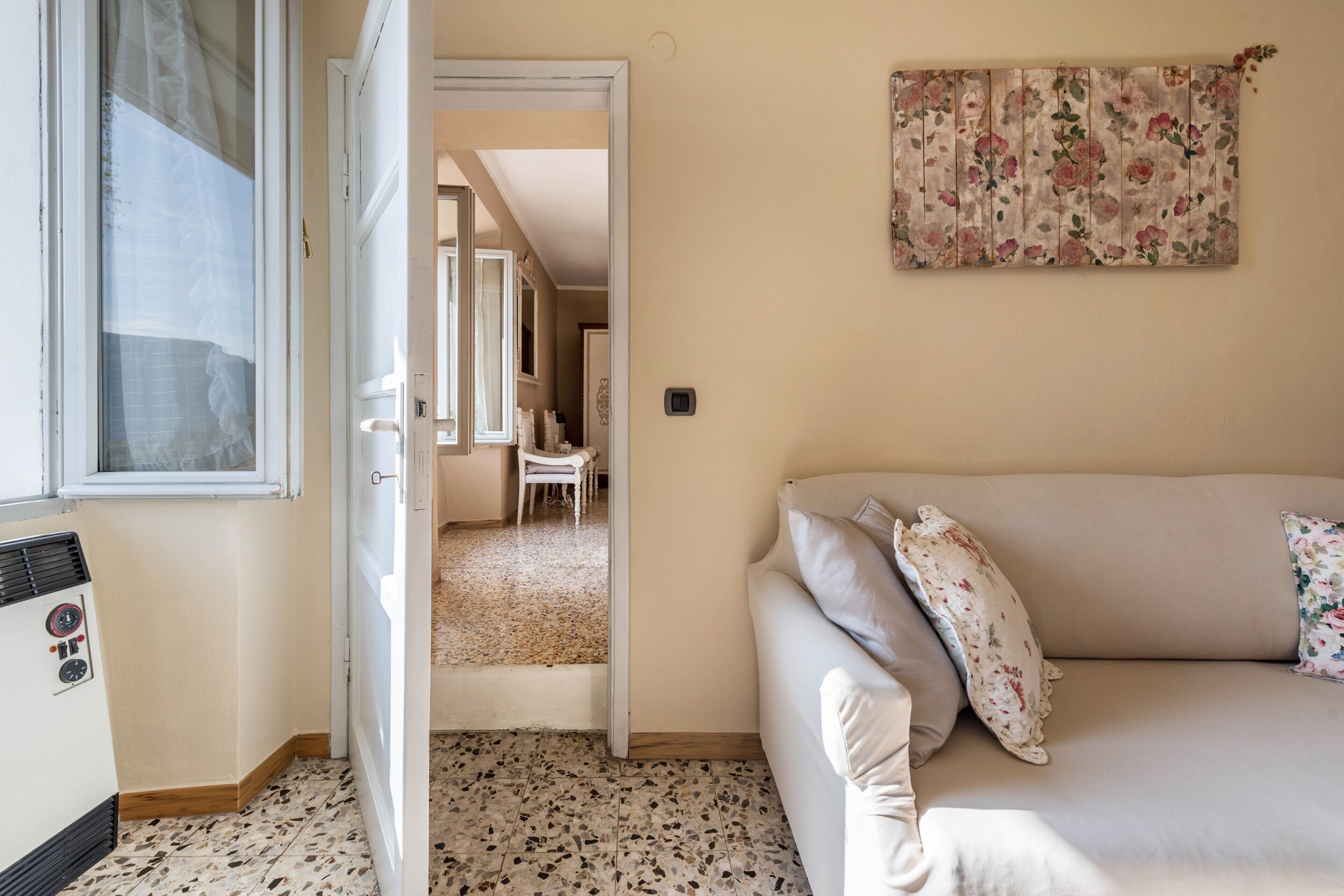 A room with a sofa, a radiator, a door leading to another room, and a wall-mounted floral tapestry.