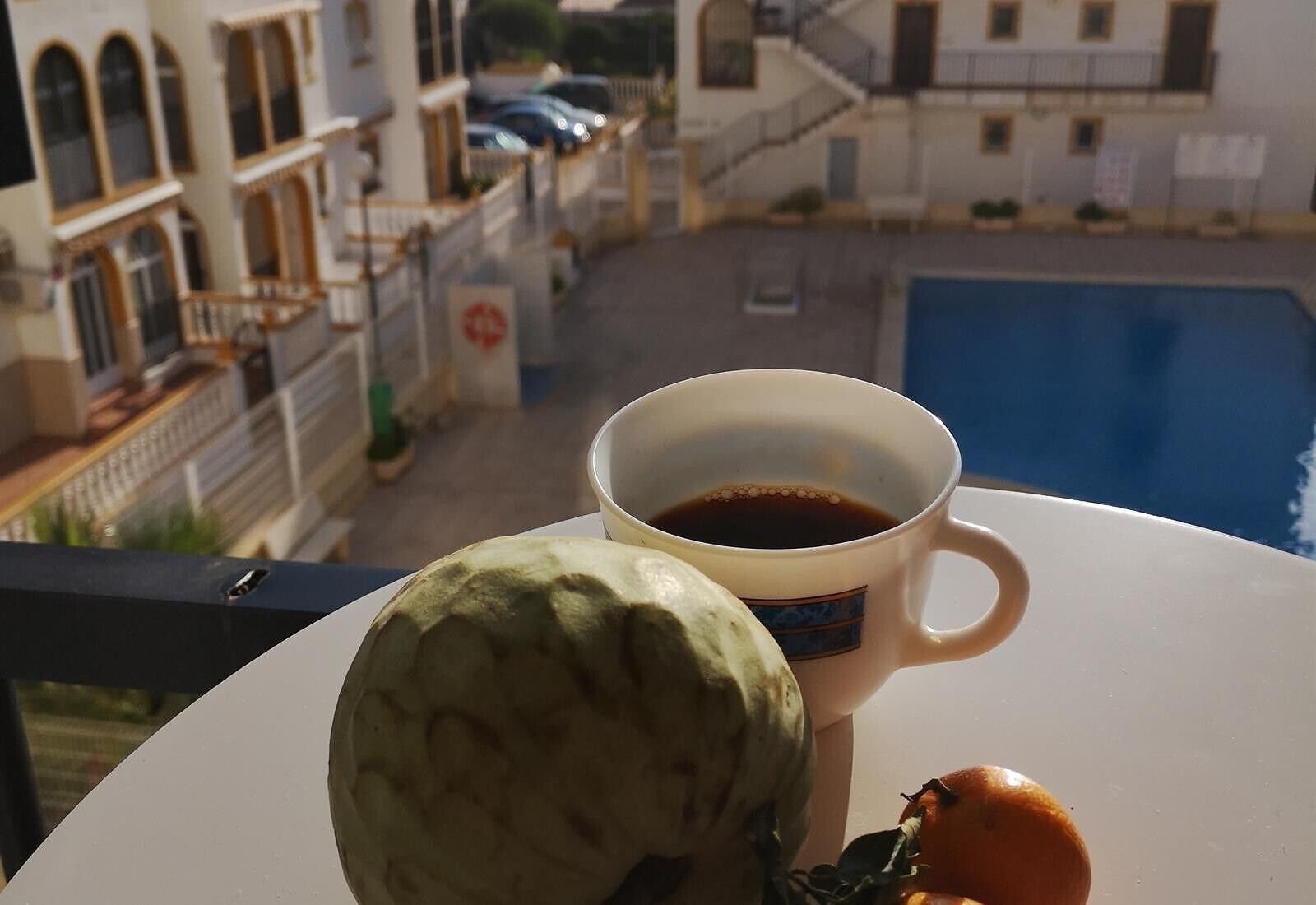 Une tasse de café sur un balcon donnant sur un quartier résidentiel avec une piscine.