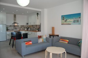 A modern living room with a grey sofa, a small round table, and a kitchen in the background.