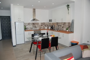Una cucina moderna con mobili bianchi, una cappa in acciaio inossidabile e una zona pranzo con tavolo in vetro e sedie nere.