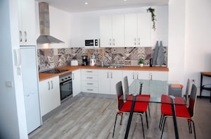 A modern kitchen with white cabinets, a microwave, a stove, and a dining area with a glass table and red chairs.