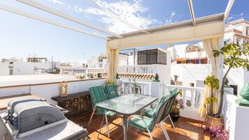 Terraza en la azotea con una mesa, sillas, una parrilla y plantas en macetas.