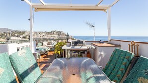Um terraço com mesa, cadeiras e vista para o mar e a cidade.