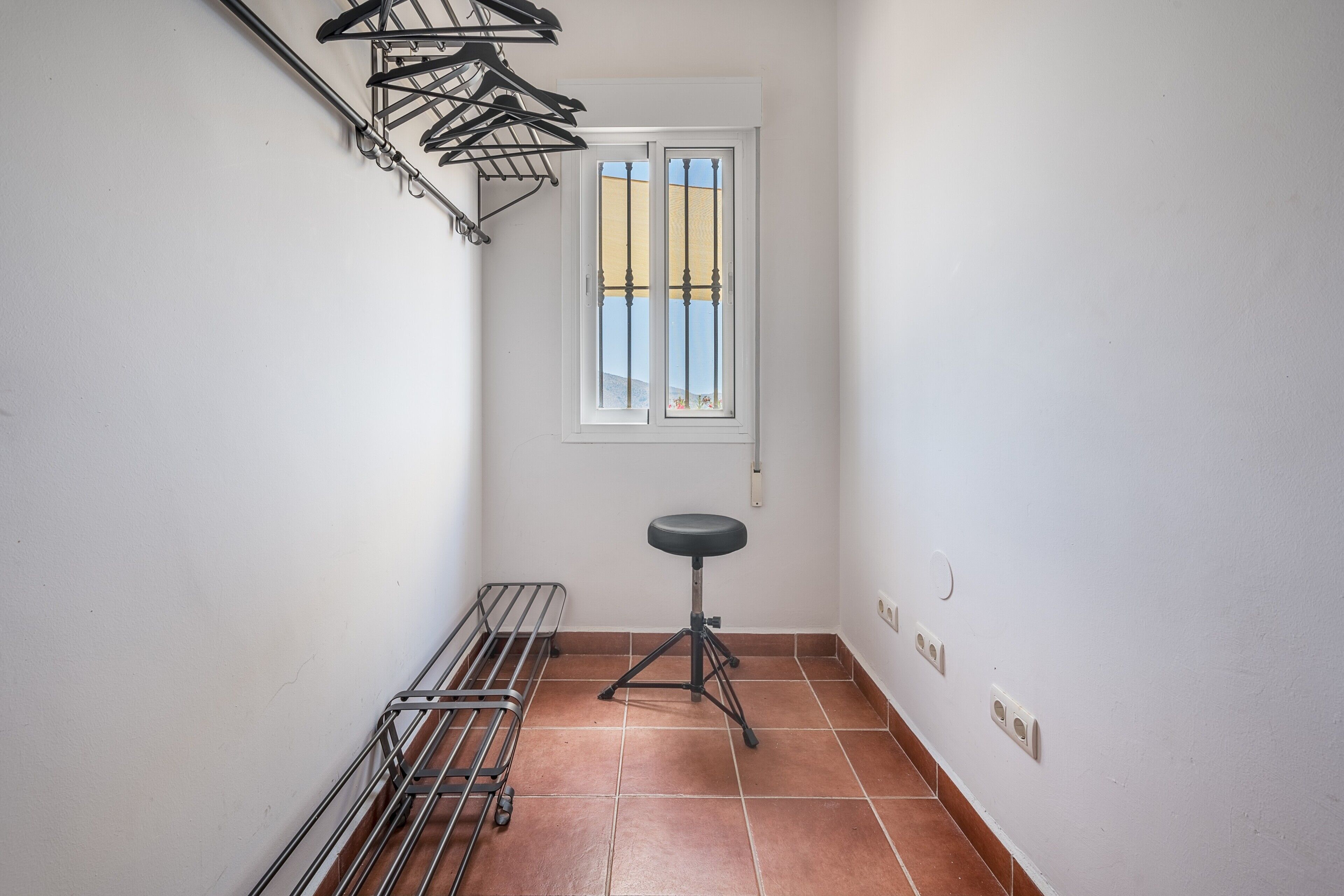A narrow hallway with a metal drying rack, a stool, and a window with a view.