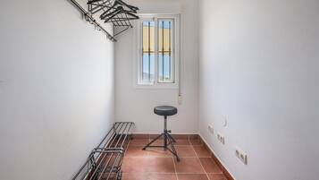A narrow hallway with a metal drying rack, a stool, and a window with a view.
