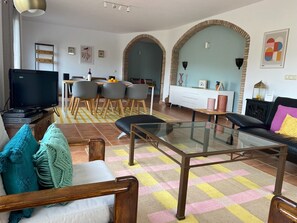 A living room with a TV, sofa, glass coffee table, and a dining area with chairs and a table.