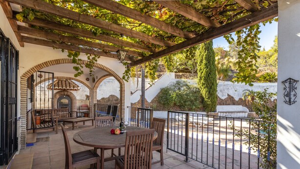 A patio with a round wooden table and chairs, a brick oven, and a pergola with climbing vines. - Villa Casa Cristina with Mountain Views, Pool, Garden, Air Conditioning and Wi-Fi (Jete)