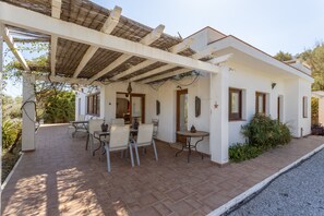 Un portico coperto con posti a sedere all'aperto, un pergolato e un edificio bianco con finestre.