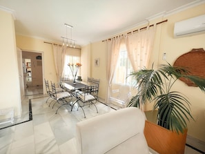 A dining area with a glass table, metal chairs, a vase with flowers, and a large potted plant.