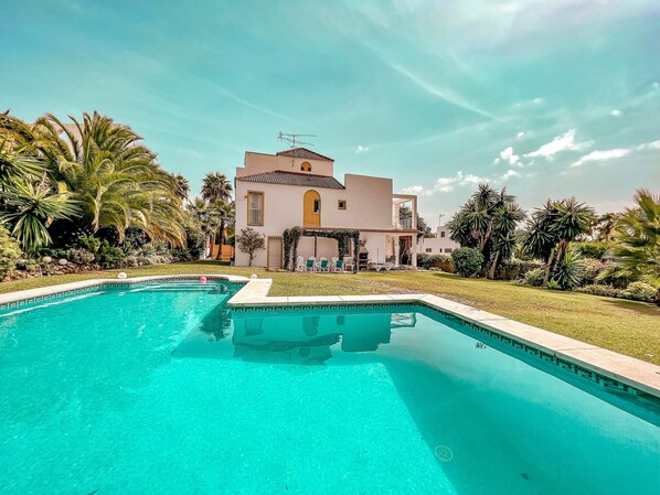 A pool with a clear blue water, surrounded by a well-maintained lawn and palm trees.