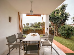 An outdoor patio with a table and chairs, a hanging lantern, and a view of greenery and buildings.