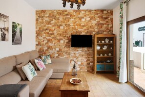 A living room with a stone wall, a sofa, a coffee table, a TV, and a tea set.