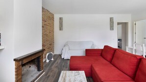 Una sala de estar con chimenea de ladrillo, un sofá blanco, un sofá rojo y una mesa de centro blanca.
