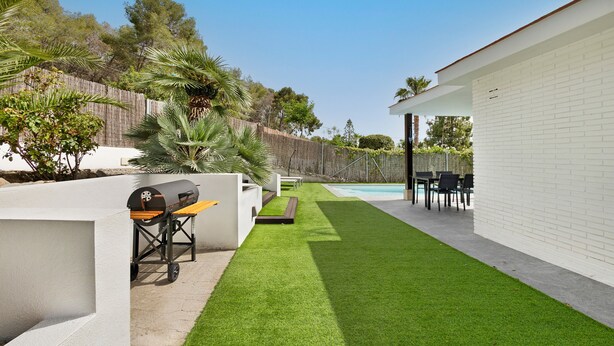 Un jardín trasero con césped artificial, una parrilla, una piscina y mobiliario exterior.