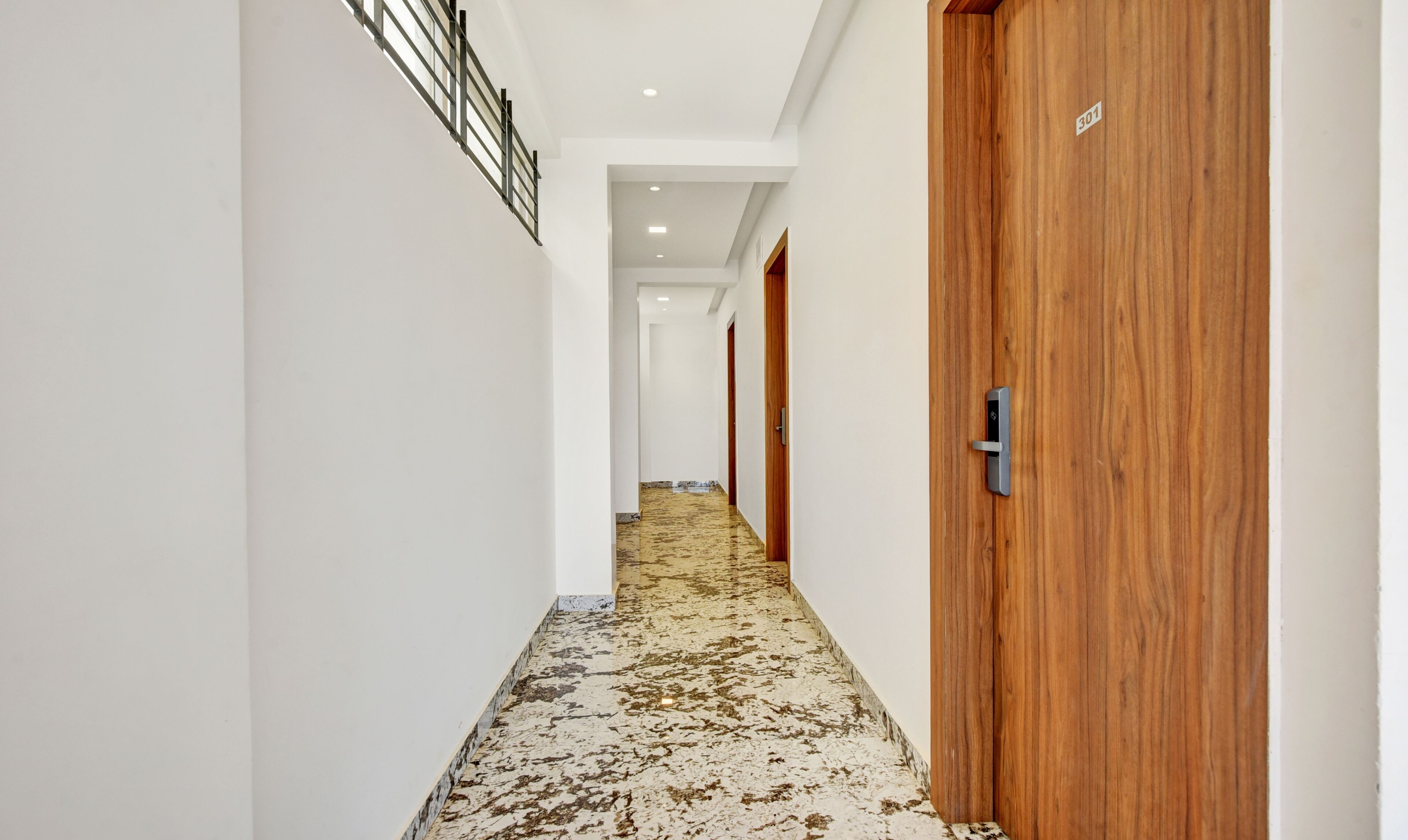 A hallway with a wooden door, a marble floor, and a white wall.