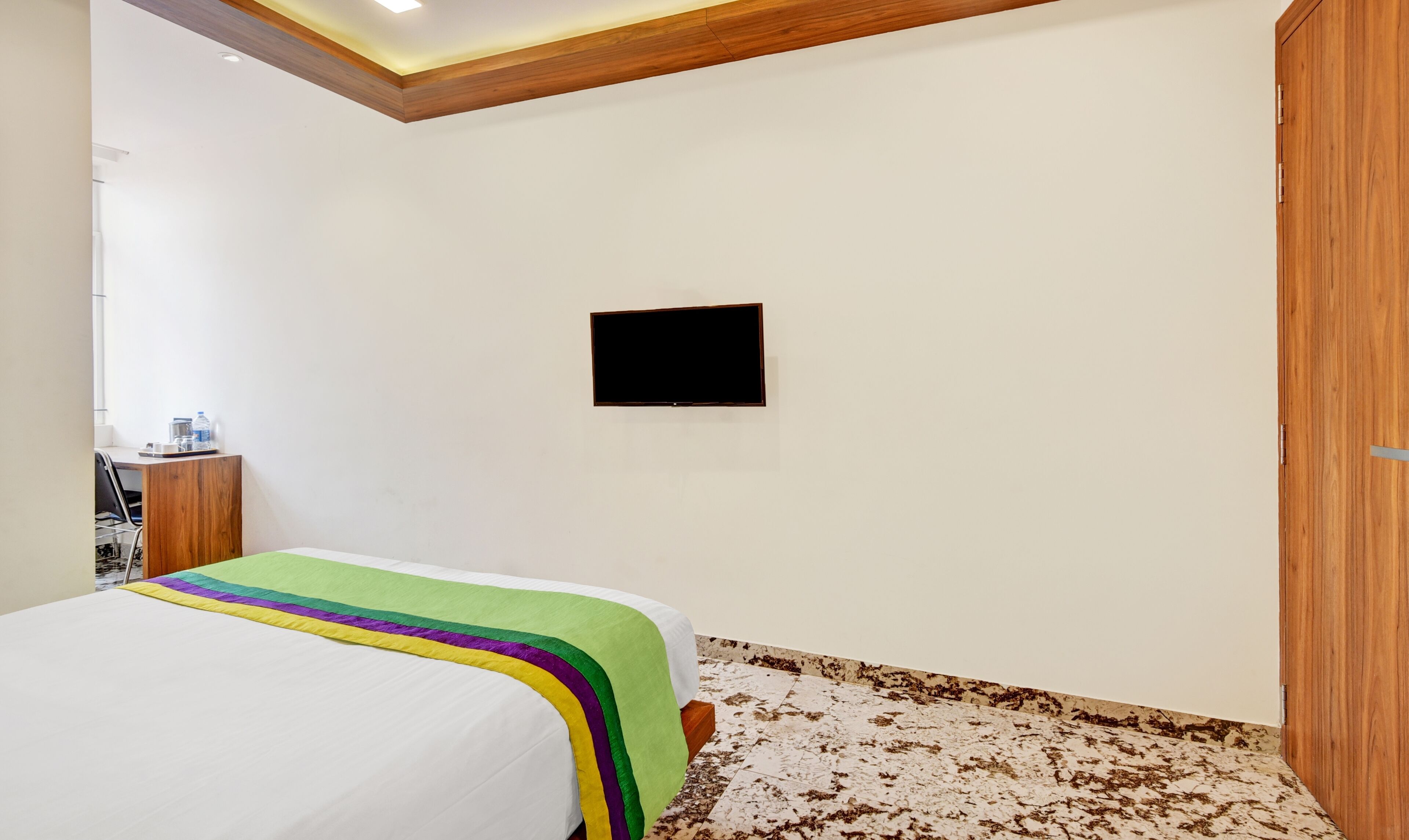 A bedroom with a bed, a flat-screen TV mounted on the wall, and a wooden wardrobe.