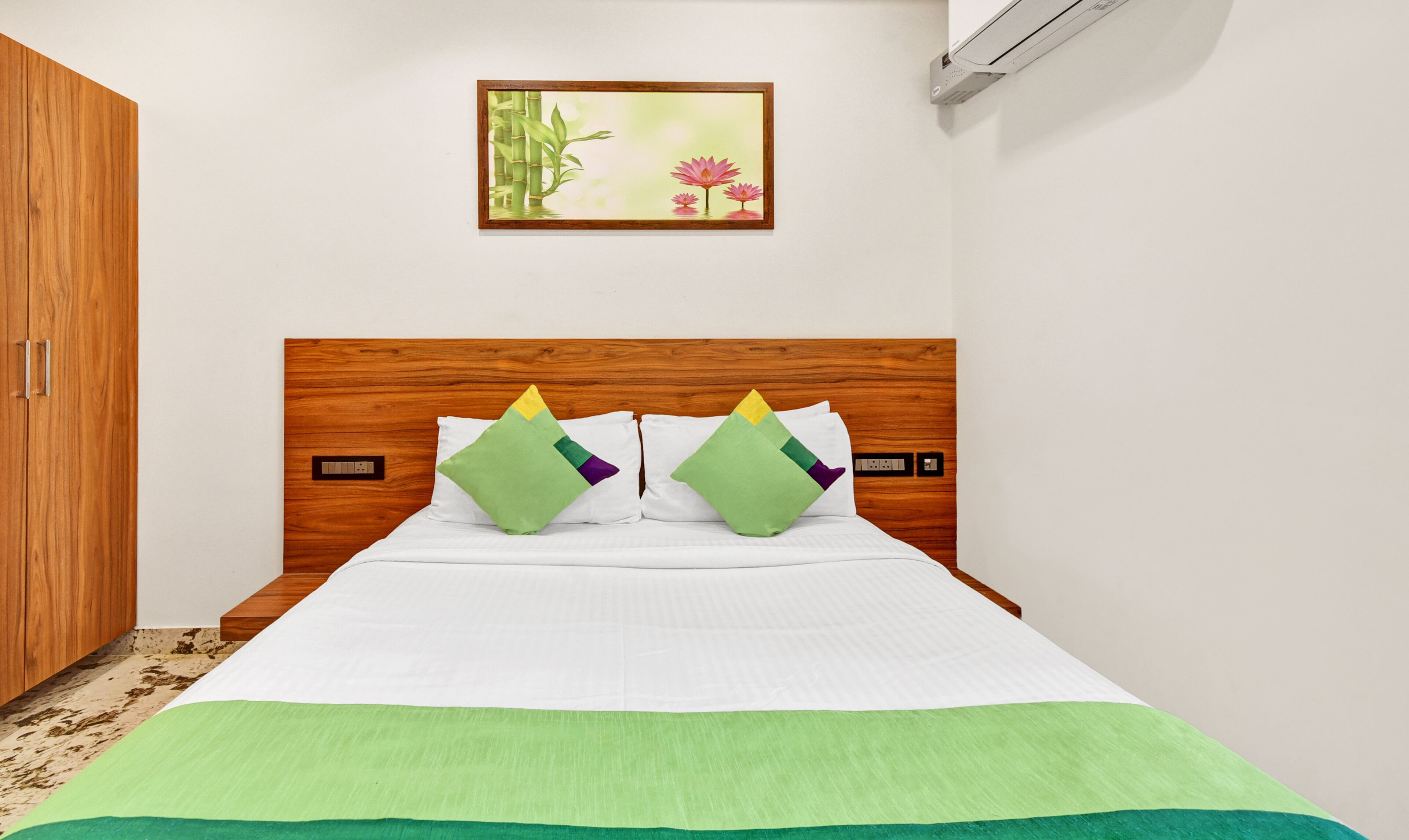 A neatly made bed with a green throw, a wooden headboard, and two pillows with geometric patterns.