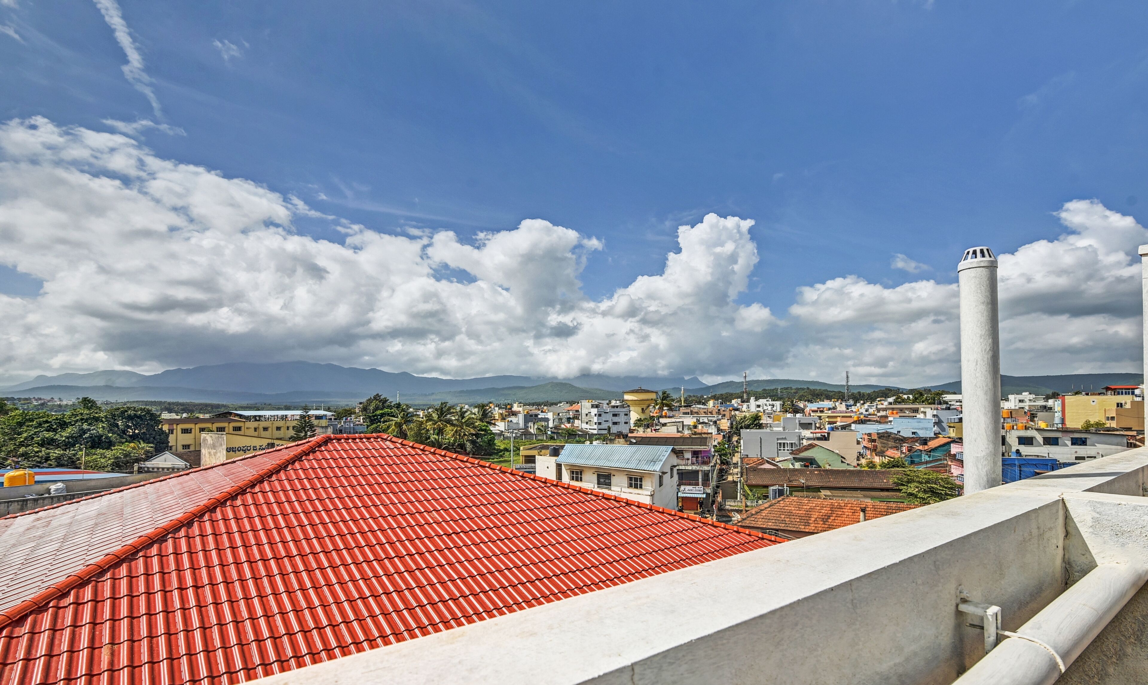 A cityscape with a prominent red-roofed building in the foreground and a view of the city and mountains in the background.